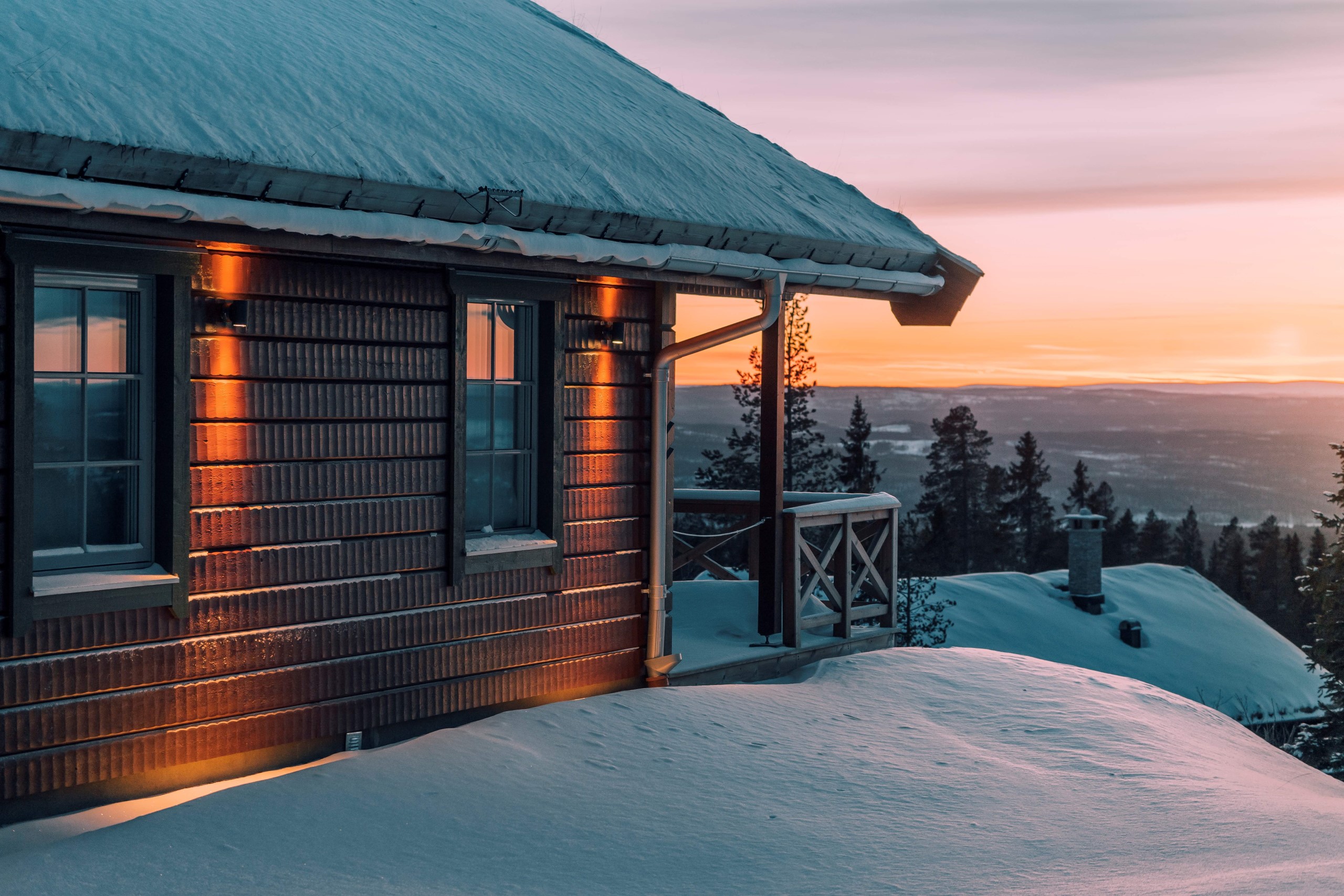 Bild på stuga i solnedgång med utsikt över fjällen.